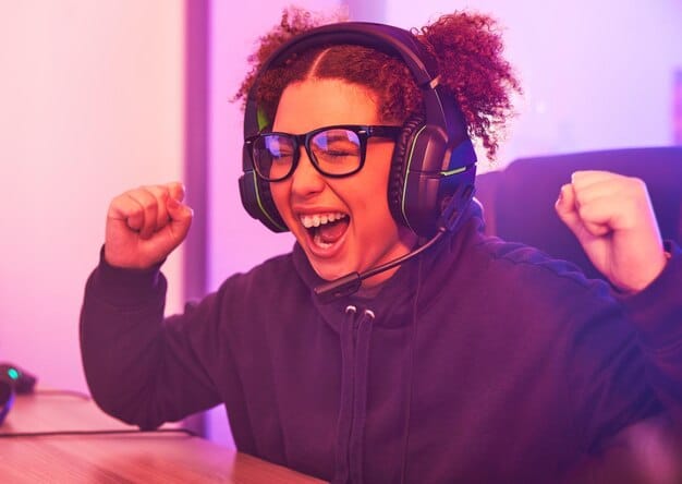 A person wearing a headset smiles widely while streaming a video game. Their face is lit by the screen, and they appear to be interacting with viewers through chat. The background includes gaming-related decor.