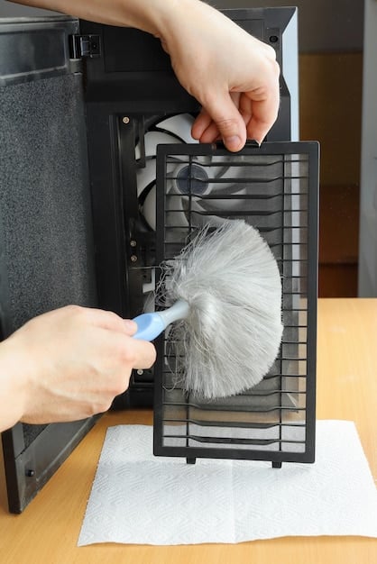 A close-up shot of a person carefully cleaning the fan of a disassembled console with a small brush and compressed air. Fine dust particles are visible being removed from the fan blades.